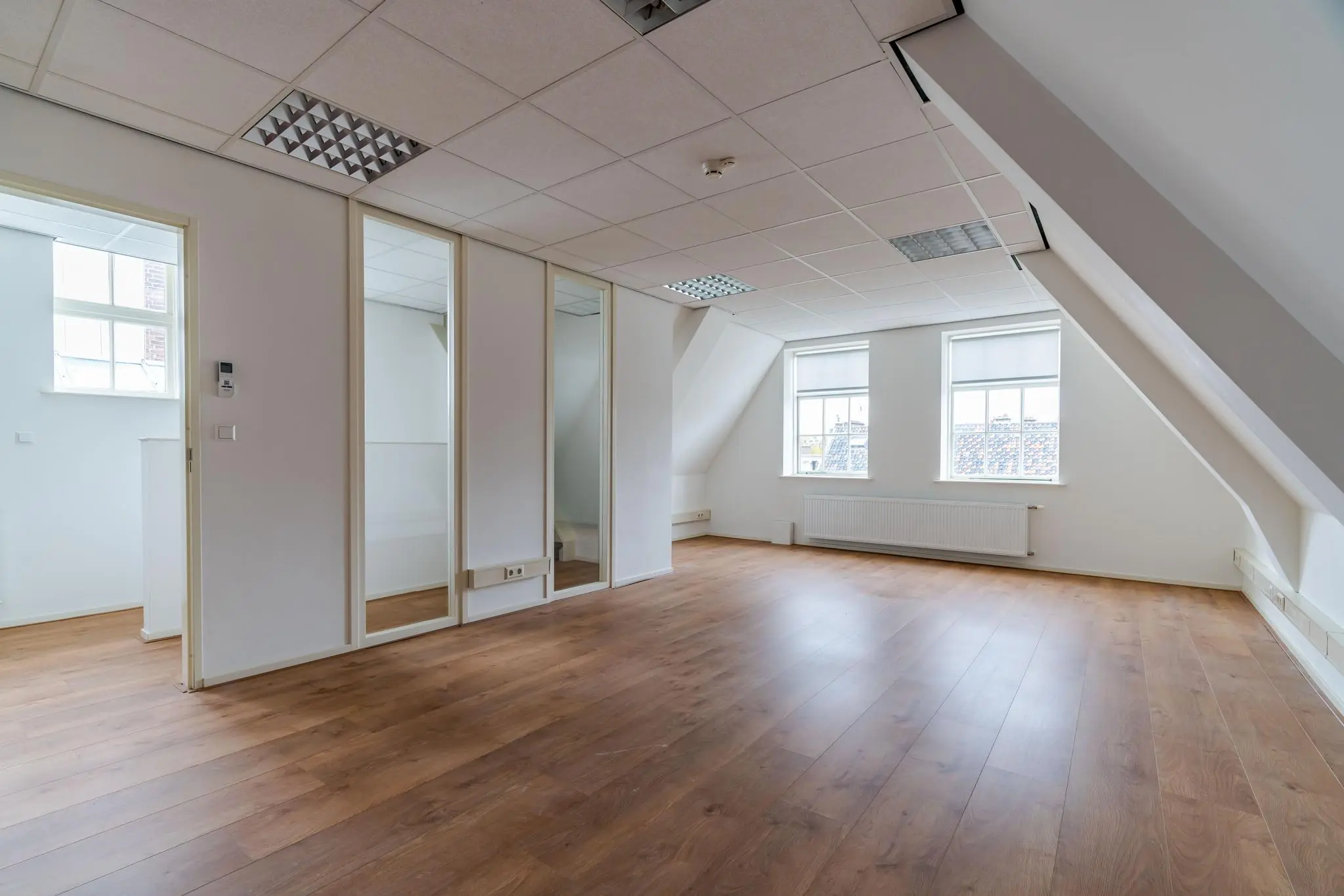 Lichte, lege zolderruimte met schuin dak, houten vloer en twee ramen in een pand aan het Lange Voorhout.